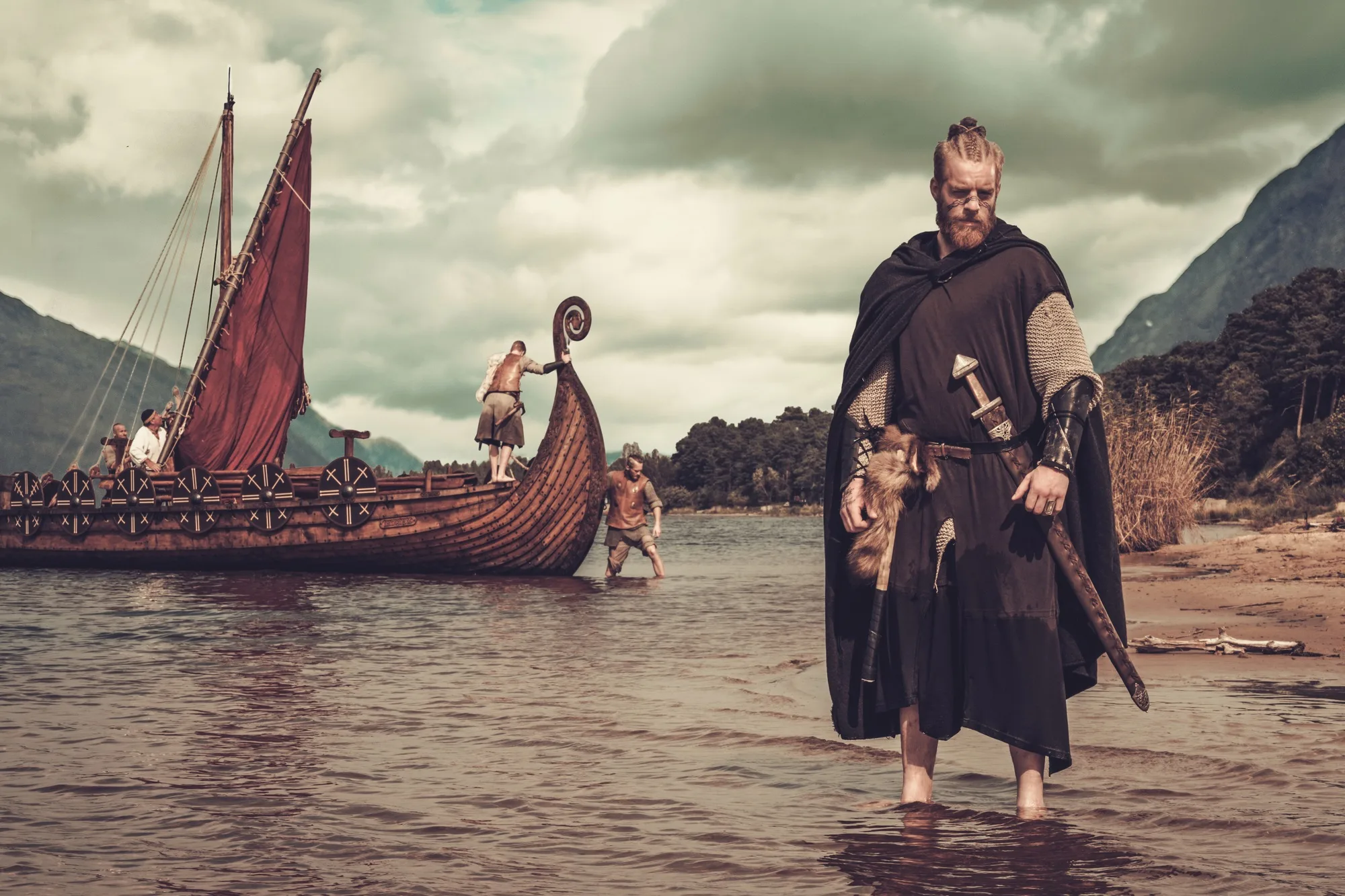 Viking warrior with sword standing near Drakkar on the seashore